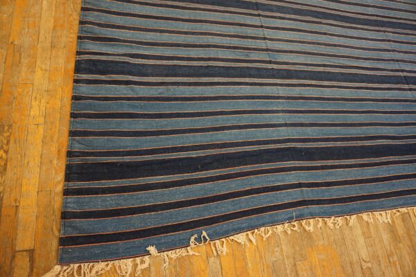 Low-profile blue and navy striped rug with peach accents and fringed ends rests on golden wood flooring.