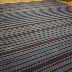 Large flatweave rug with navy and light blue stripes separated by thin orange accents on wood flooring.