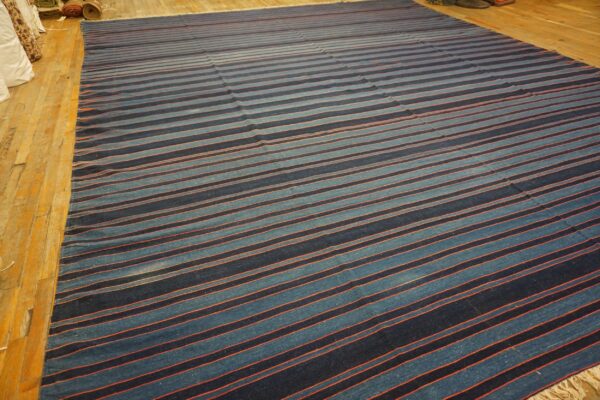 Large flatweave rug with navy and light blue stripes separated by thin orange accents on wood flooring.