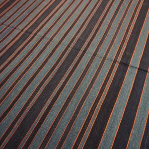 Flat-weave rug with diagonal navy, teal, and orange stripes lies on a wooden floor.