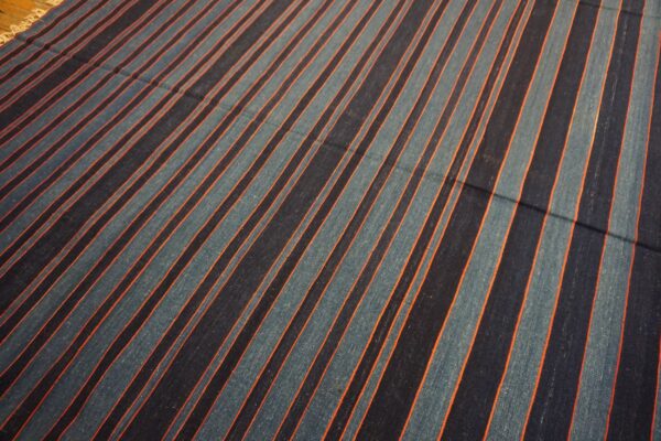 Flat-weave rug with diagonal navy, teal, and orange stripes lies on a wooden floor.