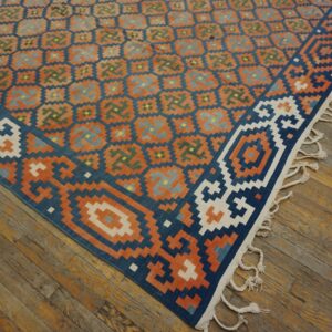 Geometric flatweave rug in blue, orange, and green rests on rustic hardwood floors, showing white fringes.