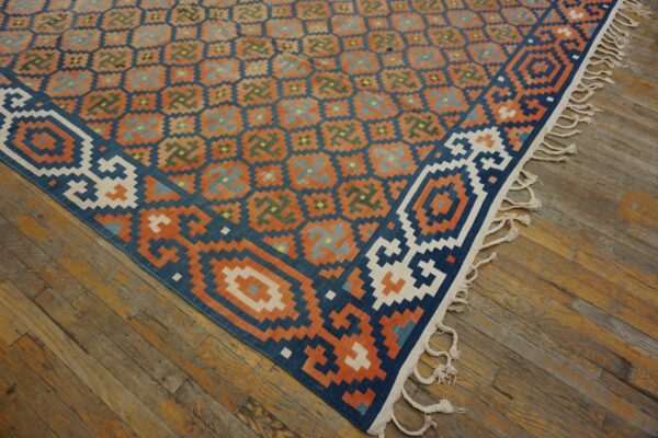 Geometric flatweave rug in blue, orange, and green rests on rustic hardwood floors, showing white fringes.