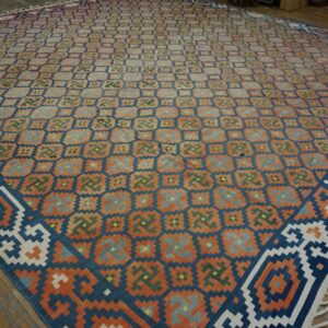 Geometric flat-weave rug with rust, navy, and teal colors covers aged wooden plank flooring.