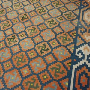 Orange and navy flat-weave rug with repeating gray and green geometric patterns laid over wood flooring.