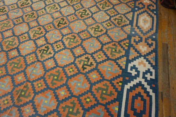 Orange and navy flat-weave rug with repeating gray and green geometric patterns laid over wood flooring.