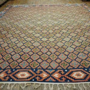 Large flatweave rug with peach, navy, and multi-colored stepped geometric patterns covers a wooden floor.