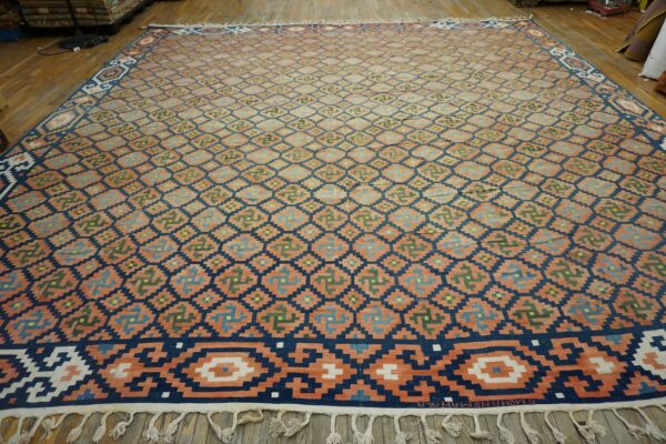 Large flatweave rug with peach, navy, and multi-colored stepped geometric patterns covers a wooden floor.