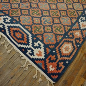 Geometric flatweave rug in navy, coral, white, and accent colors rests on rustic wooden plank flooring.