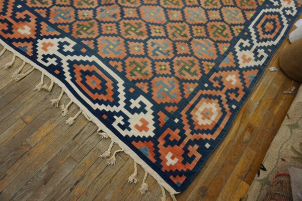 Geometric flatweave rug in navy, coral, white, and accent colors rests on rustic wooden plank flooring.
