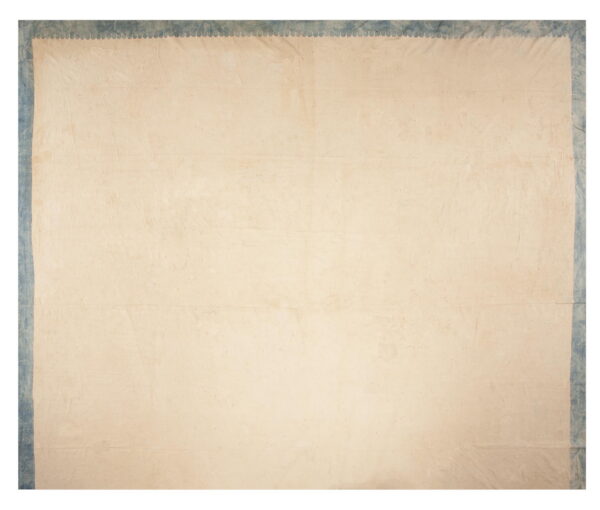 Cream rug with a scalloped edge detail separating the creased field from the textured blue border.