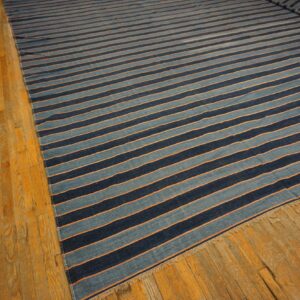 Wide striped rug in dark blue, light blue, and thin orange, laid flat on golden hardwood flooring.