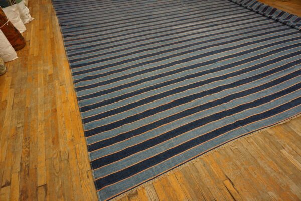 Wide striped rug in dark blue, light blue, and thin orange, laid flat on golden hardwood flooring.