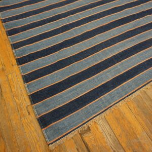 Blue striped flat-weave rug with orange details and fringe rests on golden distressed wood floor.