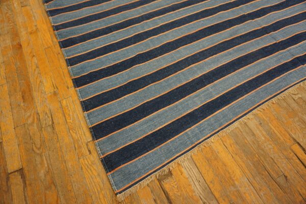 Blue striped flat-weave rug with orange details and fringe rests on golden distressed wood floor.