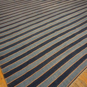 Flatwoven rug with alternating light blue and dark blue stripes separated by orange lines on wood flooring.