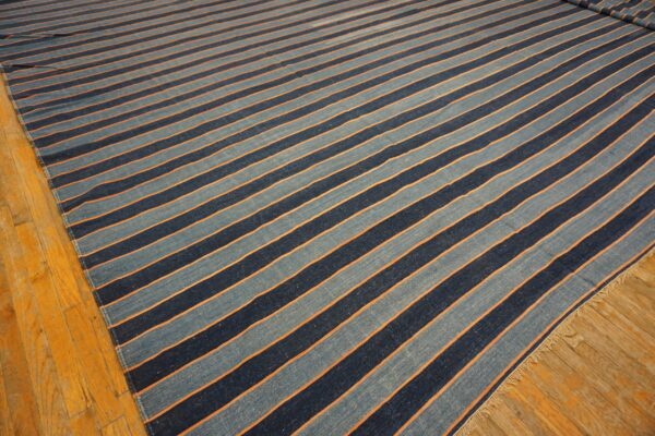 Flatwoven rug with alternating light blue and dark blue stripes separated by orange lines on wood flooring.