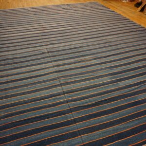 A flatweave rug with alternating blue and thin orange stripes is displayed on a polished wood floor.