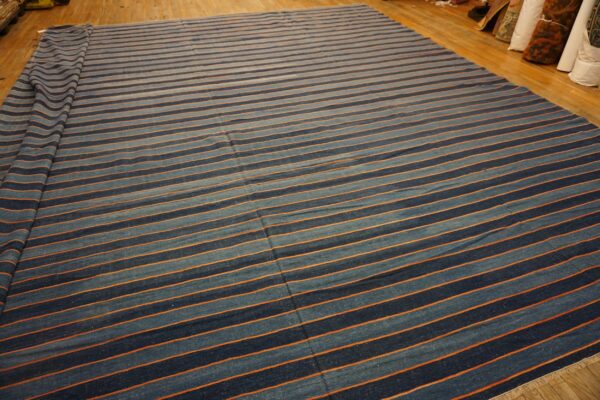 A flatweave rug with alternating blue and thin orange stripes is displayed on a polished wood floor.
