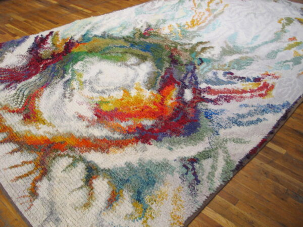High-pile rug with an abstract multicolor swirling pattern on a cream background, lying on wood floors.