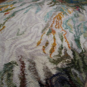 Textured, shaggy rug with an abstract painterly design in green, rust, and teal colors on wood flooring.