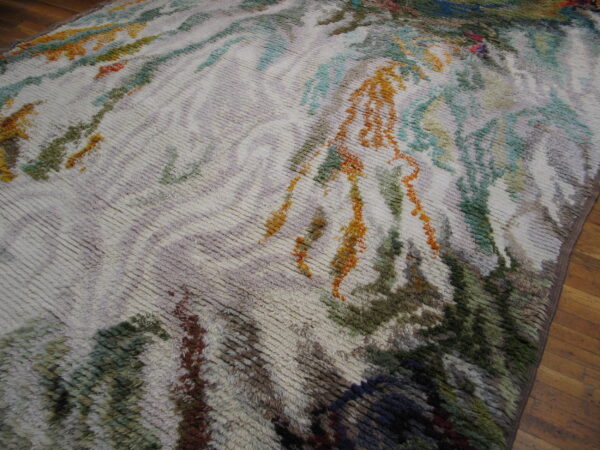 Textured, shaggy rug with an abstract painterly design in green, rust, and teal colors on wood flooring.