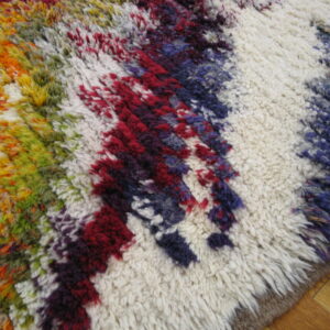 High-pile shaggy rug displaying jagged multicolored stripes over a cream base, resting on wood flooring.