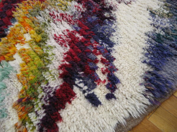 High-pile shaggy rug displaying jagged multicolored stripes over a cream base, resting on wood flooring.