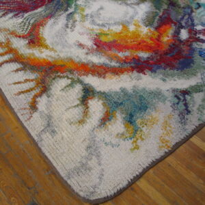 Textured white rug with abstract bursts of red, yellow, and blue colors sits on hardwood flooring.