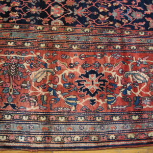 Intricate floral rug border in rust, navy, and teal surrounding a dark field, visible over hardwood.