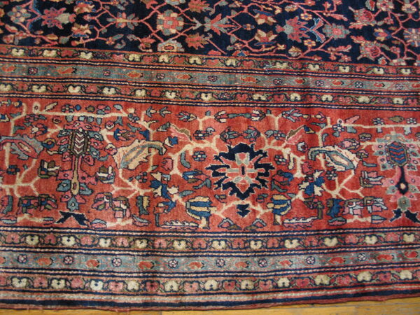 Intricate floral rug border in rust, navy, and teal surrounding a dark field, visible over hardwood.