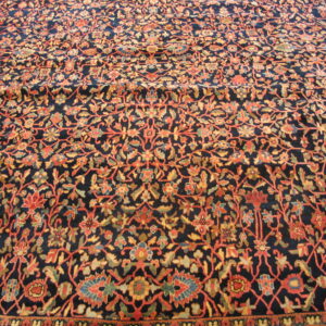 Close up of a navy blue rug with a dense floral vine pattern in orange, gold, and green.