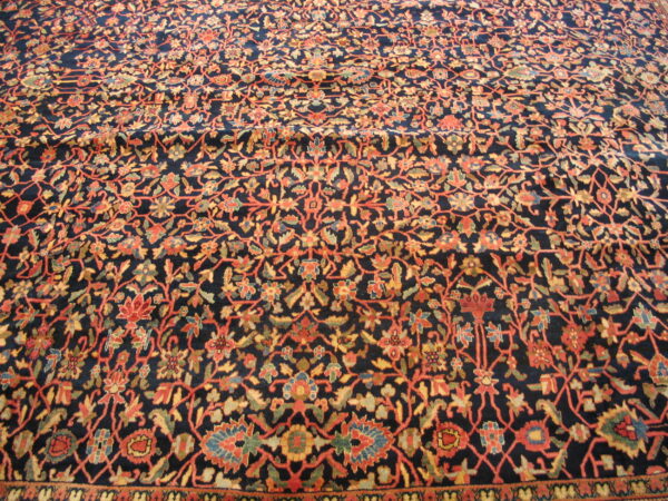 Close up of a navy blue rug with a dense floral vine pattern in orange, gold, and green.