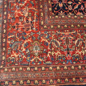 A corner section of a red and blue rug showing complex floral motifs and intricate multi-layered borders.