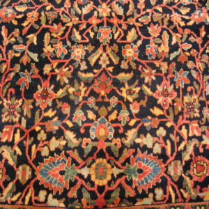 Navy rug close-up showing a dense floral pattern of rust, gold, green, and blue accents.