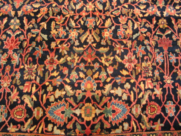 Navy rug close-up showing a dense floral pattern of rust, gold, green, and blue accents.