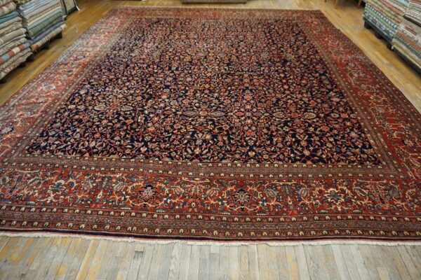 Large dark blue rug with dense floral pattern and wide red border on light wood floors.