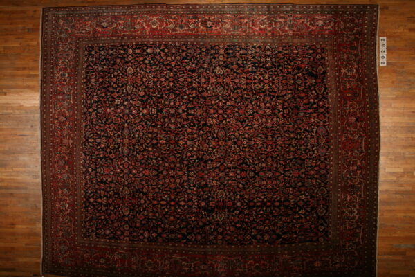 Black field rug with dense red and rust botanical designs and a prominent red border on wood floors.