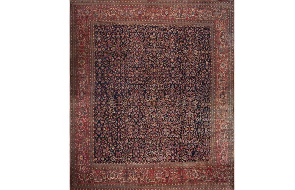 Traditional rug featuring an all-over floral pattern on a navy blue field with wide red borders.