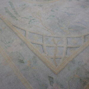 Muted blue and cream rug detail showing a floral pattern and a geometrically accented border corner.