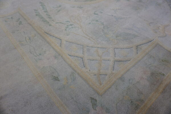 Muted blue and cream rug detail showing a floral pattern and a geometrically accented border corner.