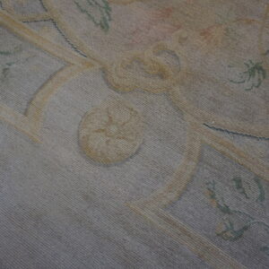 Detail of a faded, low-pile rug featuring a traditional ornamental pattern in gray, pale yellow, and muted green.