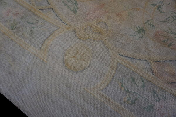 Detail of a faded, low-pile rug featuring a traditional ornamental pattern in gray, pale yellow, and muted green.