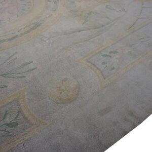 Close-up of a dense, low-pile rug with a distressed formal pattern in muted gray, yellow, and faded pink.