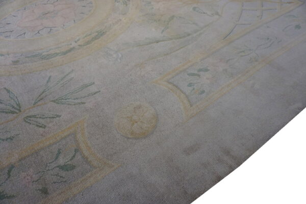 Close-up of a dense, low-pile rug with a distressed formal pattern in muted gray, yellow, and faded pink.
