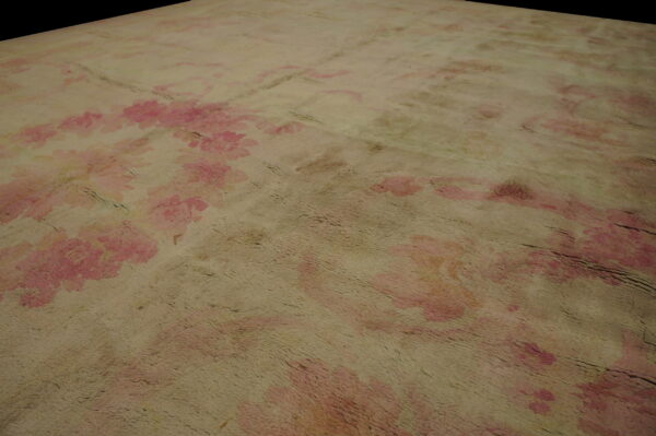 Angled view of a shaggy, textured rug with distressed pink floral motifs on a tan ground.