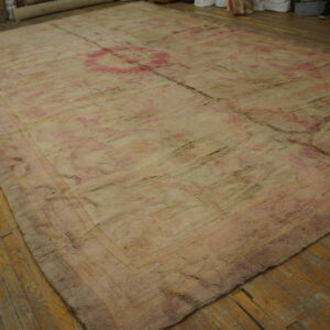 Distressed, textured rug in faded cream and rose with subtle patterns laid on a worn wood floor.