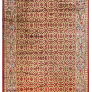 Gold rug with a repeating red geometric lattice pattern and a detailed floral tapestry border.