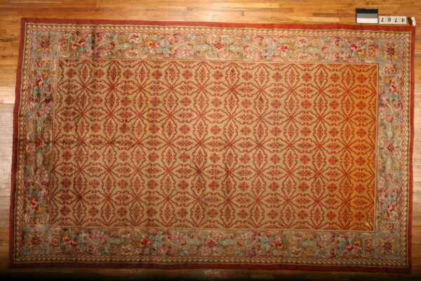 Golden-tan rug with red trellis pattern and detailed multi-color floral border on a hardwood floor.