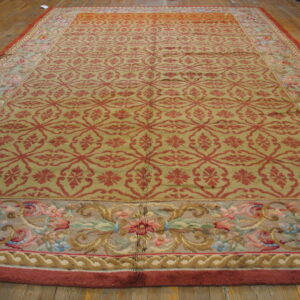 Large rug with a red geometric pattern on an olive field and wide multicolored floral borders on wood floor.